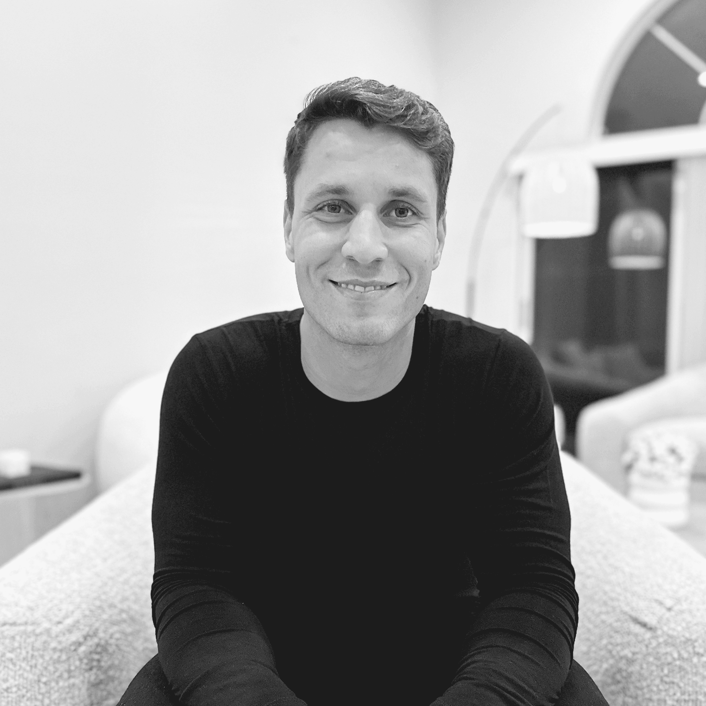 Smiling man in a black long-sleeved shirt posing for a black and white portrait.
